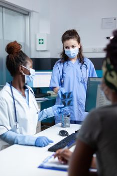 Therapist asisstant giving xray to african american radiologist doctor examining lungs disease during clinical appointment in hospital office. Medical team with protective face masl against covid19