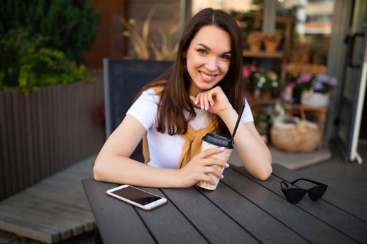 smiling young woman freelancer drinking coffee on cafe terrace.