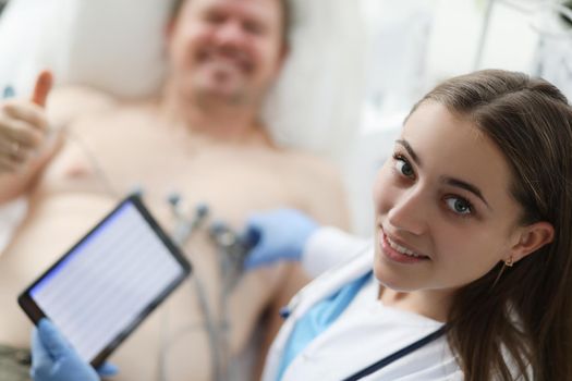 Doctor cardiologist holding digital tablet with electrocardiogram on background of patients with ok gesture. Qualitative examination of cardiovascular system concept