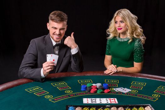 couple playing poker at the green table. The blonde girl and a guy in a suit. happy win, two aces