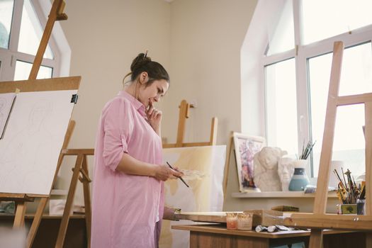 Female artist working in studio. Creative workspace, painting class, easel with canvas, art therapy. Inspiration, creativity, talent, craft concept. Artist studio interior. People, leisure and hobby.