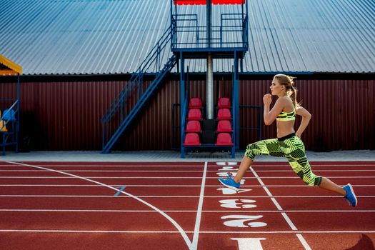 Young, beautiful girl athlete in sportswear runs along the treadmill. Sport background. Outdoor stadium
