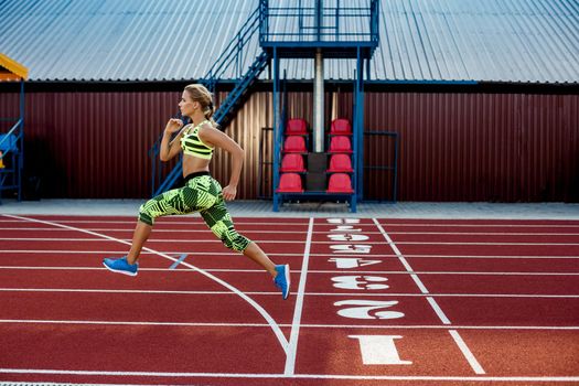Young, beautiful girl athlete in sportswear runs along the treadmill. Sport background. Outdoor stadium