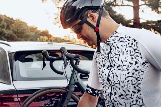 Male cyclist loading his bicycle on a rack of his crossover car after a ride