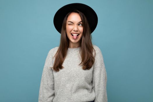 Portrait of nice good looking attractive pretty young happy positive brunette woman wearing casual striped sweater isolated over colorful background with copy space winking and showing tongue.