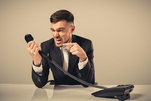 A young man in a black suit dials the phone number while sitting in the office. Manager talking on the phone. Man emotionally shouts