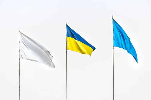 Three flags: Ukrainian national, white and blue against the grey sky.