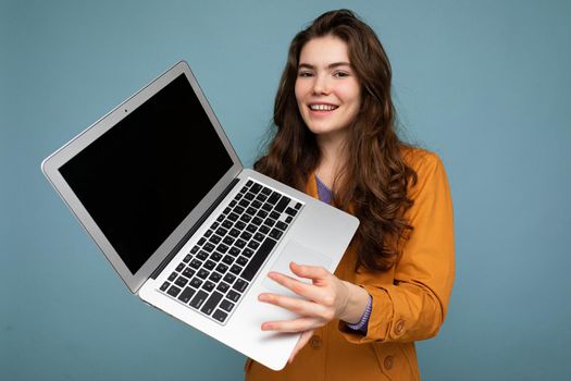 Photo of Beautiful smiling happy young woman holding computer laptop looking at camera having fun wearing casual smart clothes isolated over wall background. Mock up