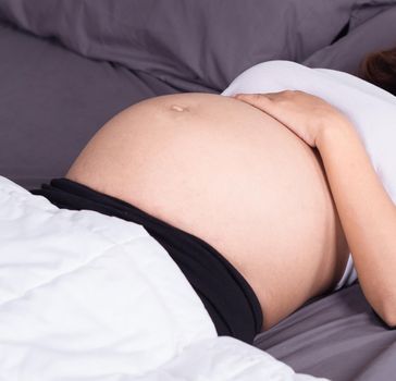 close up belly of pregnant woman sleeping on bed in the bedroom at home