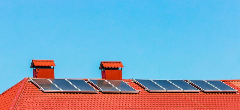 Solar panels on the red tiled roof of a building or house against a blue light sky.