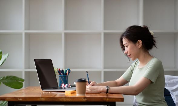 Cropped photo of woman writing making list taking notes in notepad working or learning on laptop indoors- educational course or training, seminar, education online concept.