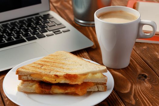 Triangle sandwich on wooden office table with laptop and coffee cup close up
