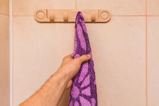 Man's hand takes an purple towel in the bathroom. Care and hygiene concept.