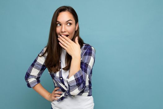 Photo of young positive happy shocked attractive pretty brunet woman with sincere emotions wearing stylish check shirt standing isolated on blue background with empty space.