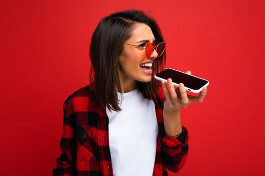 brunette on the background of a red wall speaks on the speakerphone on the phone, angry.