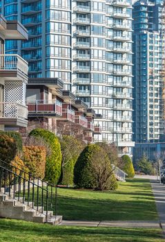 Facades of residential apartment buildings with doorsteps from the green lawn in front. Low-rise condo building on high-rise tower backgfound