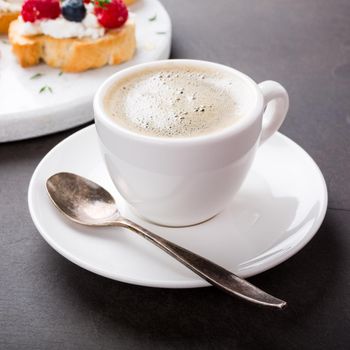 Cup of coffee with berry and goat cheese sandwiches on marble cutting board, top view, copy space.