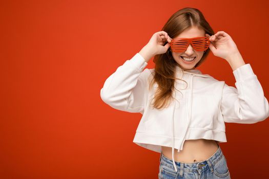 Photo shot of beautiful positive young blonde woman wearing casual clothes and stylish optical glasses isolated over colorful background wall looking at camera. copy space