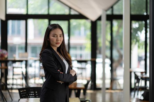 Portrait of successful young Asian businesswoman at office, She standing and looking at camera wears a black suit