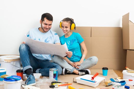 Happy boy and girl in protective headphones sitting on floor with blueprint. Home remodeling after moving. Construction tools and materials for building. Couple having fun in time of house renovation