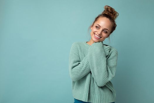 Young beautiful cute curly blonde woman with sexy expression, cheerful and happy face wearing trendy blue sweater isolated over blue background with copy space.