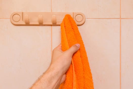 Man's hand takes an orange towel in the bathroom. Care and hygiene concept.