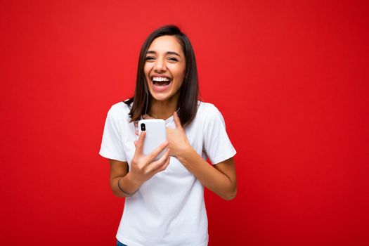 Photo of attractive crazy amazed surprised young woman wearing casual stylish clothes standing isolated over background with copy space holding and using mobile phone looking at camera.