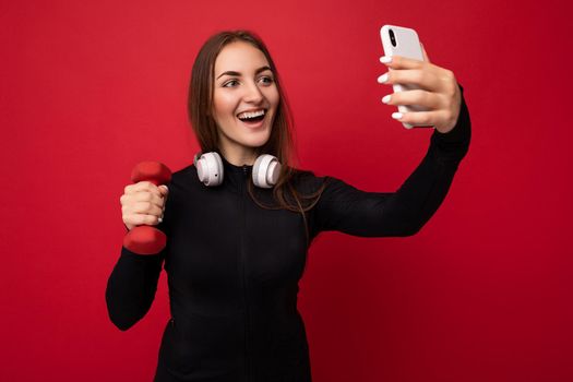 Attractive charming young smiling happy woman holding and using mobile phone taking selfie wearing stylish clothes isolated over wall background.