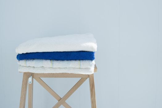 stack of clean bath towels colorful cotton Terry textile stacked on wooden chair near white wall pile concept closeup country style