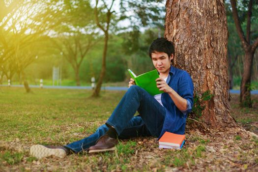 young man sitting and reading a book in the park