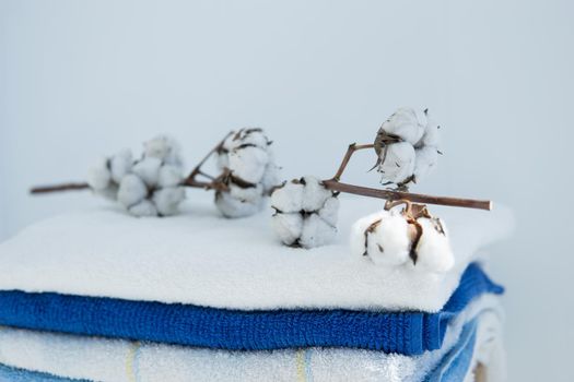 stack of clean bath towels colorful cotton Terry textiles with a sprig of cotton folded on a wooden chair against a white wall nap concept close-up country style