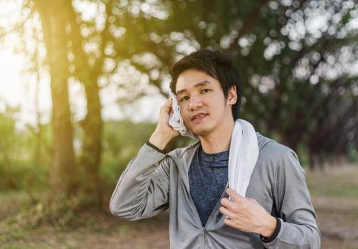 young sporty man resting and wiping his sweat with a towel after workout sport exercises outdoors at the park