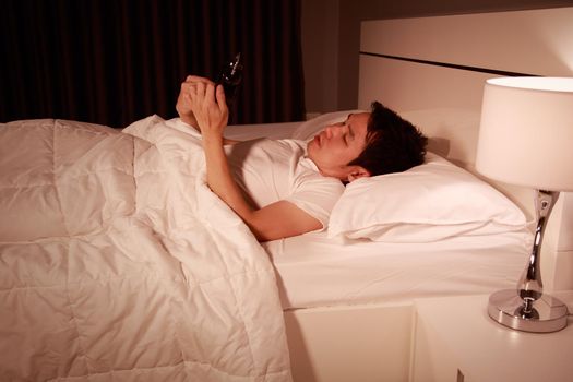 young man using his mobile phone in bed at night