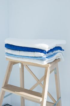 stack of clean bath towels colorful cotton Terry textile stacked on wooden chair near white wall pile concept closeup country style