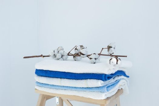 stack of clean bath towels colorful cotton Terry textiles with a sprig of cotton folded on a wooden chair against a white wall nap concept close-up country style.