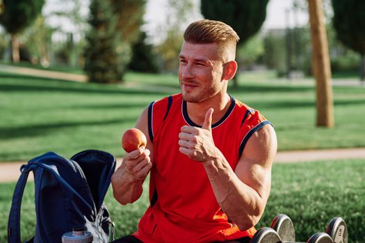 man in the park sits on a bench and eats an apple summer. High quality photo