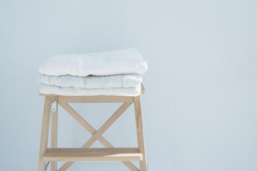 stack of clean bath towels colorful cotton Terry textile stacked on wooden chair near white wall pile concept closeup country style