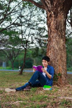 young man sitting and reading a book in the park