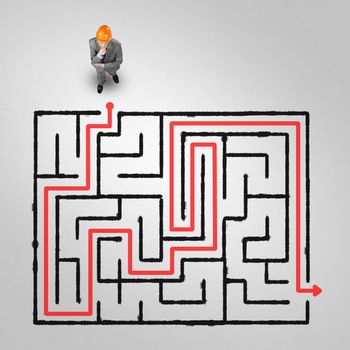Top view of puzzled businessman in helmet looking at drawn maze on floor