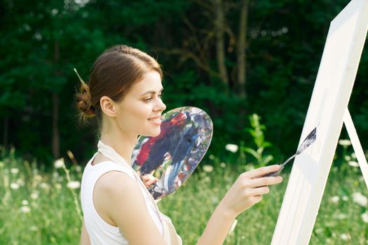 woman artist outdoors with palette of paints paints a picture. High quality photo