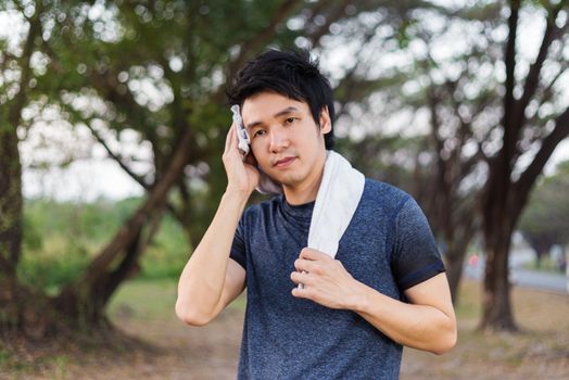 young sporty man resting and wiping his sweat with a towel after workout sport exercises outdoors at the park