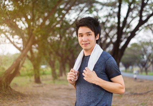 young sporty man with white towel resting after workout sport exercises outdoors at the park