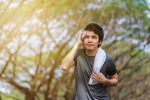 young sporty man running and wiping his sweat with a towel in the park