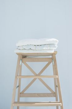 stack of clean bath towels colorful cotton Terry textile stacked on wooden chair near white wall pile concept closeup country style