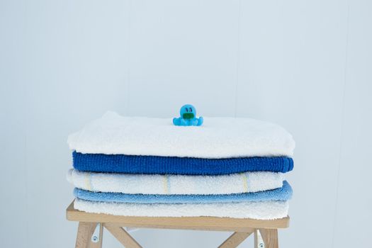 A stack of clean bath towels colorful cotton Terry textiles stacked on a wooden chair against a white wall NAP concept close up country style. Children's rubber bath toys.