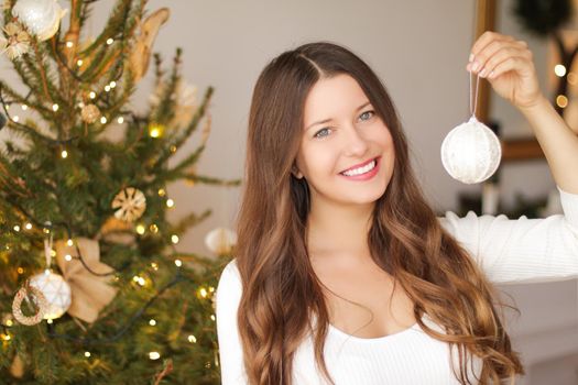 Decorating Christmas tree and winter holidays concept. Happy smiling woman holding festive ornament at home.