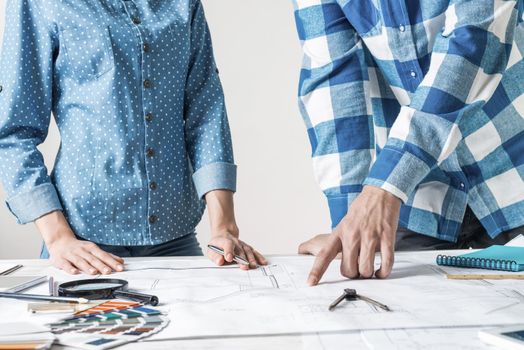 Man and woman together working at design project. Creative teamwork at workspace with construction blueprint and color swatches. People standing near desk and discussing in architecture studio.