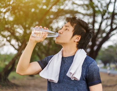 young sporty man drinking water in the park