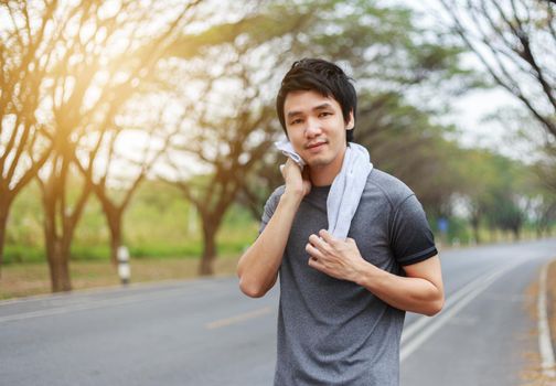 young sporty man resting and wiping his sweat with a towel after workout sport exercises outdoors at the park