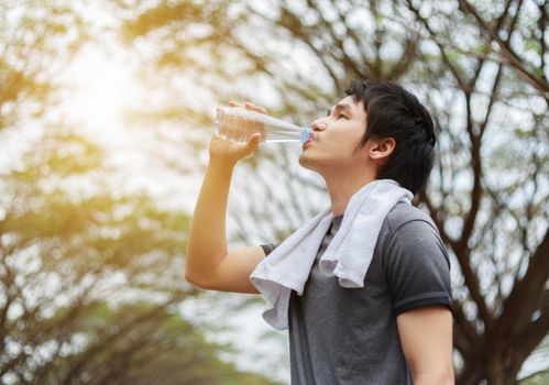 young sporty man drinking water in the park